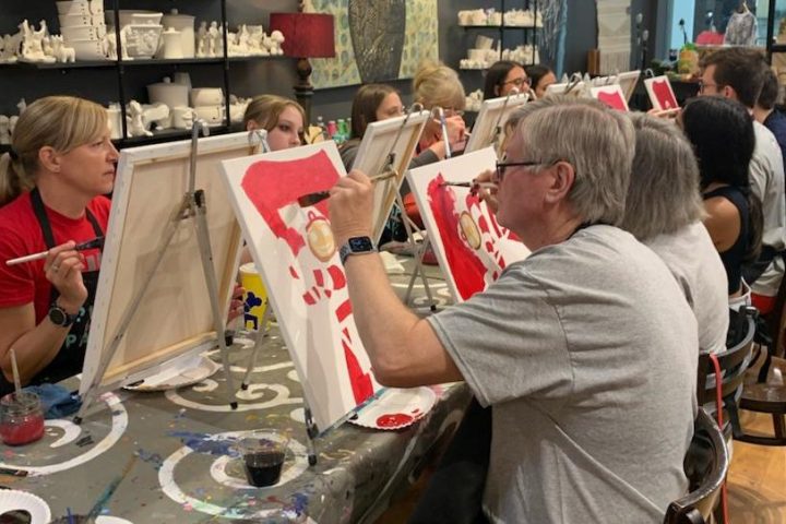 People painting on canvases in a group art class at a studio with paintings on the walls.