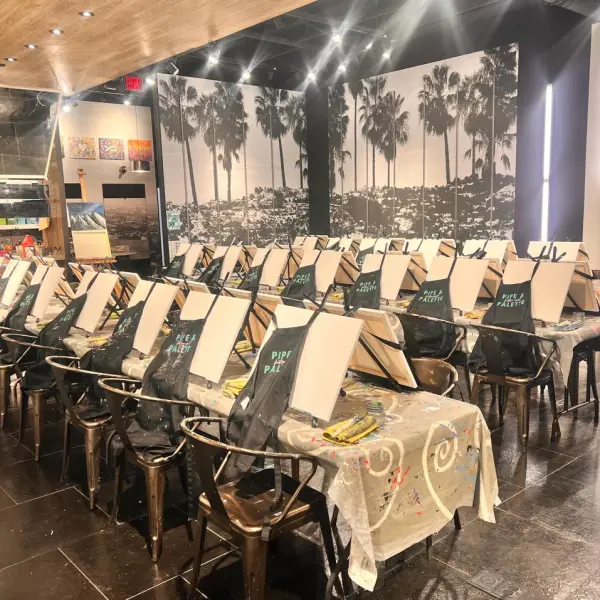Art studio with easels and aprons arranged for a painting event, palm tree mural on wall.