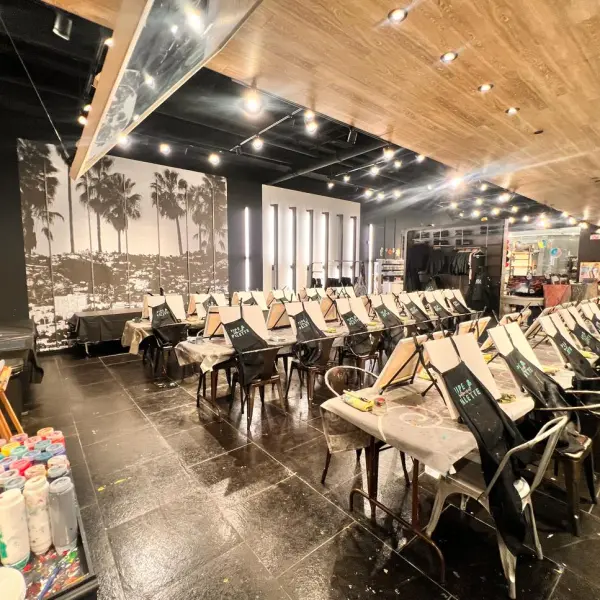 Art studio with rows of easels and paint supplies, black and white palm tree mural on wall.