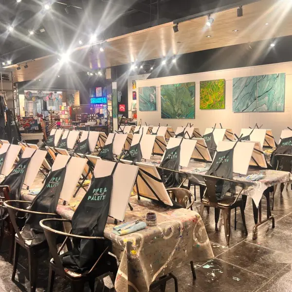Art studio with multiple easels, chairs, and aprons set up for a painting class.